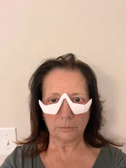 Person wearing a white eye mask against a plain background